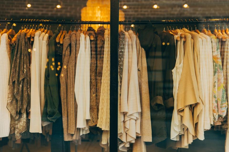 Araras com tricôs, cardigãs e blusas em tons de creme, caramelo e verde-oliva pendurados em cabides de madeira